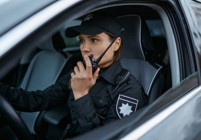Woman police officer using walkie-talkie portable radio driving in car. Female cop patrolling street